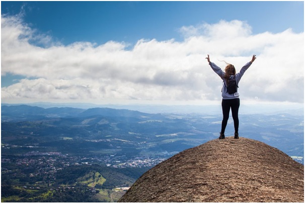 back view of woman standing on top of a rock with arms thrown in air ( less anxiety is one gratitude practice benefit)