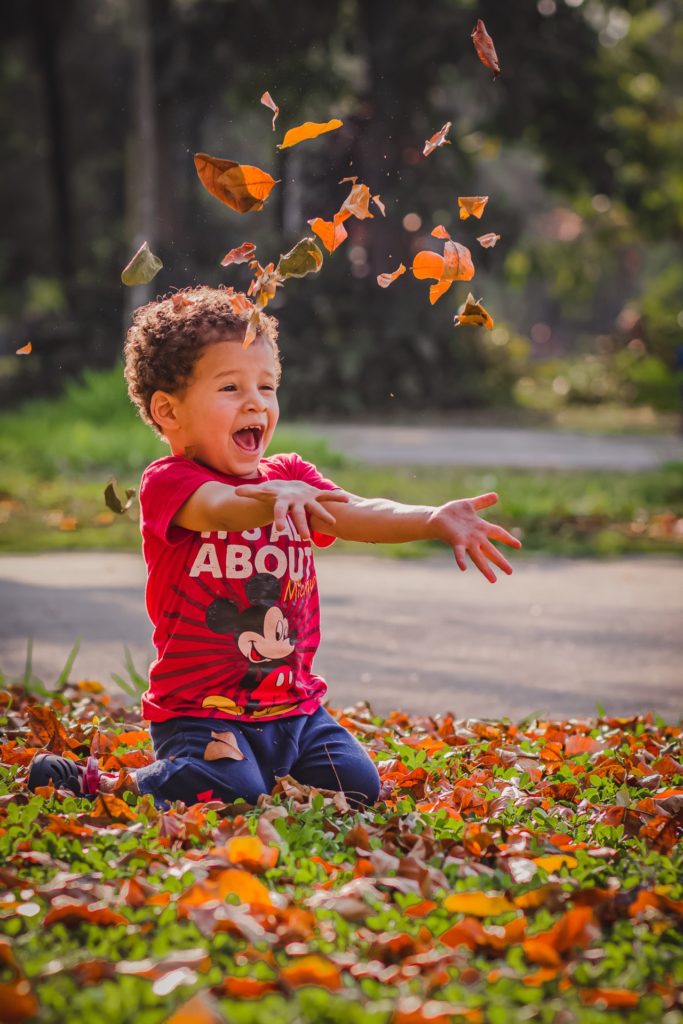 Child playing with dry leaves in a park - innocence of childhood